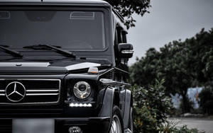 黑色 Mercedes-Benz G-Class SUV 停放在樹木附近，天空多雲。 — Mercedes Benz C300 壁紙