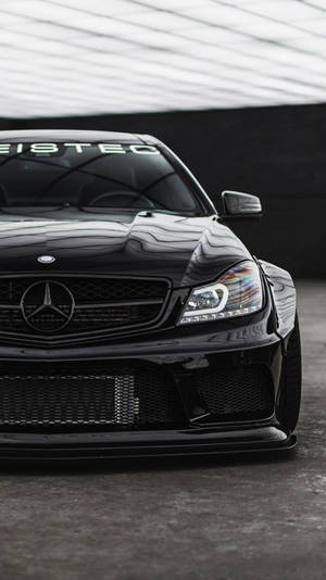 黑色 Mercedes 跑車經過自訂改裝，停放在遮陽篷下。 — Mercedes Amg iPhone 壁紙