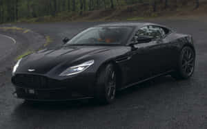黑色Aston Martin DB11在潮濕的森林道路上，黃昏時分 — Steam Deck 壁紙