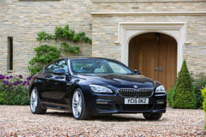 黑色BMW 6系列停在石砌莊園前，帶有拱形木門。 — Surface 壁紙