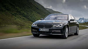 黑色BMW 7系列轎車在翠綠山丘和積雪山峰的山路上行駛。 — Mercedes Benz C300 壁紙
