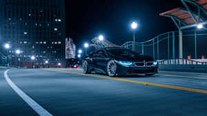 夜晚城市街道上的黑色BMW i8跑車，車頭燈和街燈閃爍。 — 7680x4320 壁紙
