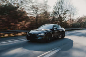 日落時分，黑色BMW M4雙門跑車在森林道路上飛馳。 — 福斯汽車 壁紙