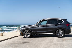 黑色BMW SUV停泊在海邊，海浪拍打著海岸。 — 黑色 BMW 壁紙