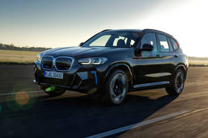 黑色BMW X3 SUV在日落時分行駛在道路上，帶有動態模糊和鏡頭光暈。 — 黑色 BMW 壁紙