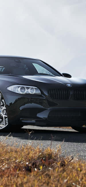 黑色BMW跑車停在瀝青路上，附近有乾草。 — Galaxy A07s 壁紙