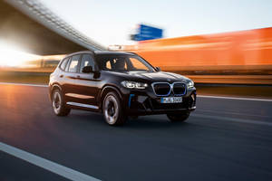黑色BMW電動SUV在日落時分的高速公路上飛馳，帶有動態模糊效果。 — 黑色 BMW 壁紙