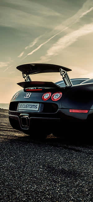 黑色Bugatti跑車配備定制尾翼，在夕陽下停放在碎石上。 — Galaxy S24 壁紙