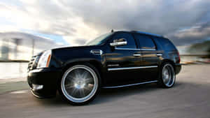 黑色Cadillac Escalade SUV在海濱道路上飛馳，帶有動態模糊效果。 — 凱迪拉克 壁紙