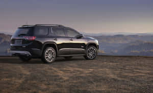 黑色GMC Acadia SUV停泊在俯瞰森林山脈的山丘上，夕陽西下。 — MacBook Pro 13 壁紙
