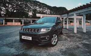 黑色Jeep Compass停放在有蓋結構下，背景有樹木。 — 混凝土 壁紙