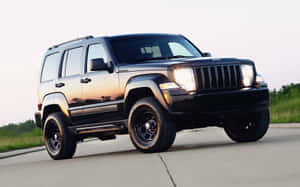 黑色Jeep Liberty SUV停在日落時分的路上，背景是草地田野。 — MacBook Pro M1 壁紙