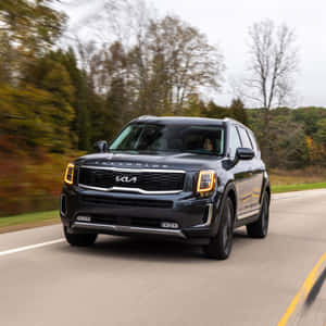 黑色Kia Telluride在秋樹環繞的道路上行駛。 — 起亞 壁紙