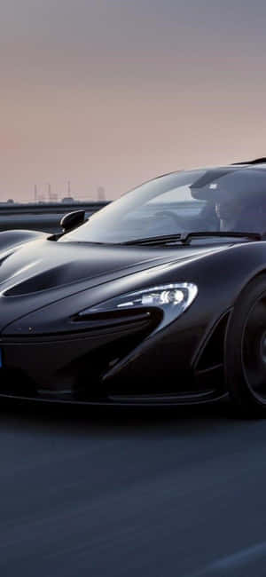 黑色McLaren跑車在暮色中的高速公路上疾馳。 — iPhone 17e 壁紙
