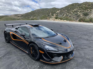 黑色McLaren跑車帶橙色飾邊停在瀝青地上，靠近山丘。 — 麥拉倫 壁紙