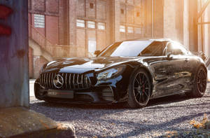 日落時分，黑色Mercedes-AMG GT停在碎石路上，前方是磚造建築。 — Mercedes-Benz 壁紙