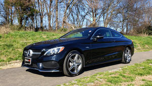 黑色Mercedes C63 AMG雙門轎跑車停泊在帶有草地和光禿樹木的道路上。 — Mercedes Benz C300 壁紙