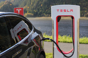 黑色Tesla汽車在湖邊和森林附近的充電站充電。 — 加油站 壁紙