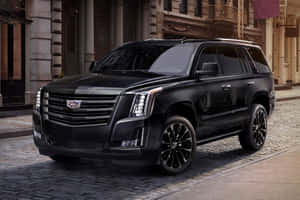 黑色凱迪拉克 Escalade SUV 停放在石砌建築附近的鵝卵石街道上。 — MacBook Air M4 壁紙