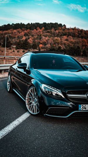 黑色梅賽德斯轎跑車停在路上，背景是秋天的樹木和藍天。 — Mercedes Amg iPhone 壁紙