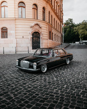 黑色經典賓士轎車在鵝卵石街道上，靠近華麗建築。 — Mercedes Benz C300 壁紙