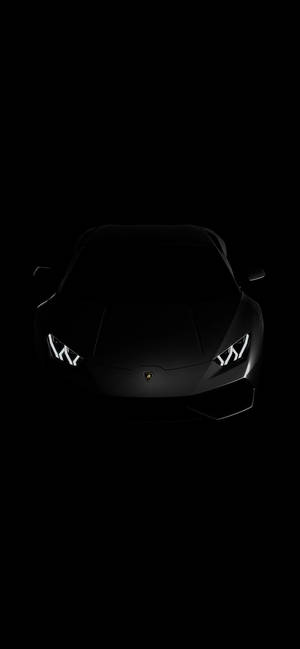 黑色藍寶堅尼跑車在黑暗中車頭燈發光。 — iPhone 16 Pro 壁紙