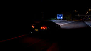 黑色跑車在夜間黑暗高速公路上疾馳，帶有發光的紅色尾燈。 — 省電 壁紙