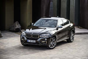 黑色BMW X6 M豪華SUV停放在現代建築附近的石路上。 — Surface Pro 壁紙