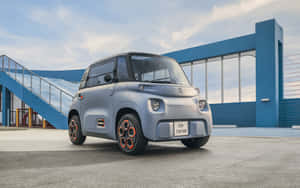 銀色未來感小型車，橙色輪圈，停在藍色工業建築前。 — 雪鐵龍 壁紙