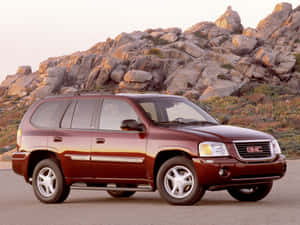 日落時分，栗色GMC Envoy SUV停放在岩石沙漠山丘附近。 — 4:3 壁紙