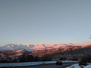 汽車在積雪道路上，山脈沐浴在日落餘暉中
