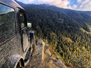 泥濘吉普車停在懸崖上，俯瞰日落時分的森林山谷 — 山景 壁紙