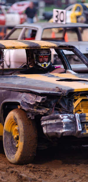 破爛的 demolition derby 賽車，車手戴著頭盔，在泥濘賽道上。 — Pixel 4 壁紙