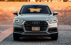 日落時分，一輛銀色 Audi Q5 SUV 停在鵝卵石車道上的正面視圖。 — MacBook Pro 13 壁紙