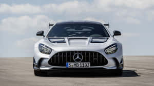 銀色 Mercedes-AMG GT R 賽車在鋪砌的賽道上，在多雲的天空下。 — Pro Display XDR 壁紙