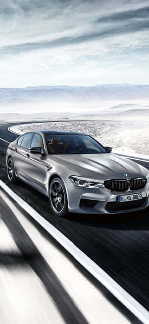 銀色BMW M5在沙漠公路上疾馳，遠山為背景。 — Galaxy A07 壁紙
