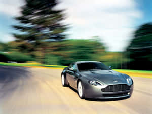 銀色跑車在彎曲道路上疾馳，背景模糊綠色。 — 奧斯頓馬丁 壁紙