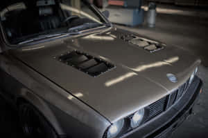 灰色BMW E30，帶有黑色引擎蓋進氣口，停放在有自然光的車庫中。 — MacBook Air 13 壁紙