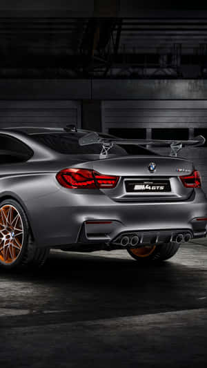 昏暗工業車庫中的消光灰色BMW M4 GTS，配備銅色輪圈。 — BMW iPhone 壁紙