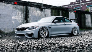 消光銀色BMW M4雙門跑車停放在碎石上，靠近混凝土牆。