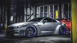 客製化銀色日產GT-R，配備藍色輪圈，停放在黑暗的工業倉庫中。