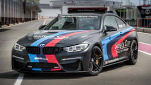 消光黑色BMW M4 Coupe安全車，帶有藍、紅、白色條紋，停在賽道上。 — 賽車 壁紙