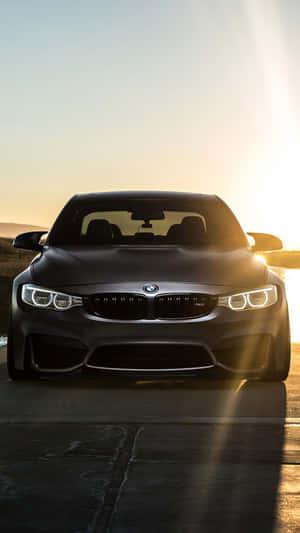 夕陽下的消光黑色BMW M4，帶鏡頭光暈 — BMW iPhone 壁紙