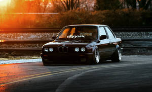 深棕色BMW E30甩尾車在金色日落時分停在潮濕的道路上。 — 福斯汽車 壁紙