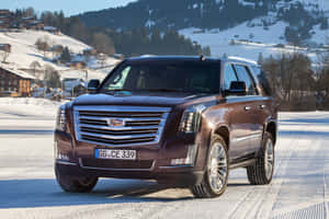 深棕色Cadillac SUV在阿爾卑斯山村附近的積雪山路上。 — Surface Laptop 壁紙