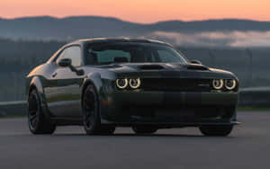 深綠色Dodge Challenger SRT Hellcat在日落時分的賽道上，背後有霧氣繚繞的山脈。 — 道奇 壁紙