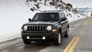 深綠色Jeep Patriot在積雪的山路上行駛，帶有黃色標線。 — 吉普 壁紙