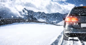 冬季降雪時，深色SUV在積雪的山路上行駛。 — 冬季風景 壁紙