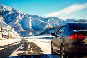深色汽車停放在積雪的道路上，背景是白雪覆蓋的山巒。 — 冬季風景 壁紙
