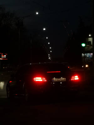 一輛汽車的紅色尾燈在路燈下的潮濕城市街道上夜間發光。 — Mercedes Benz C300 壁紙